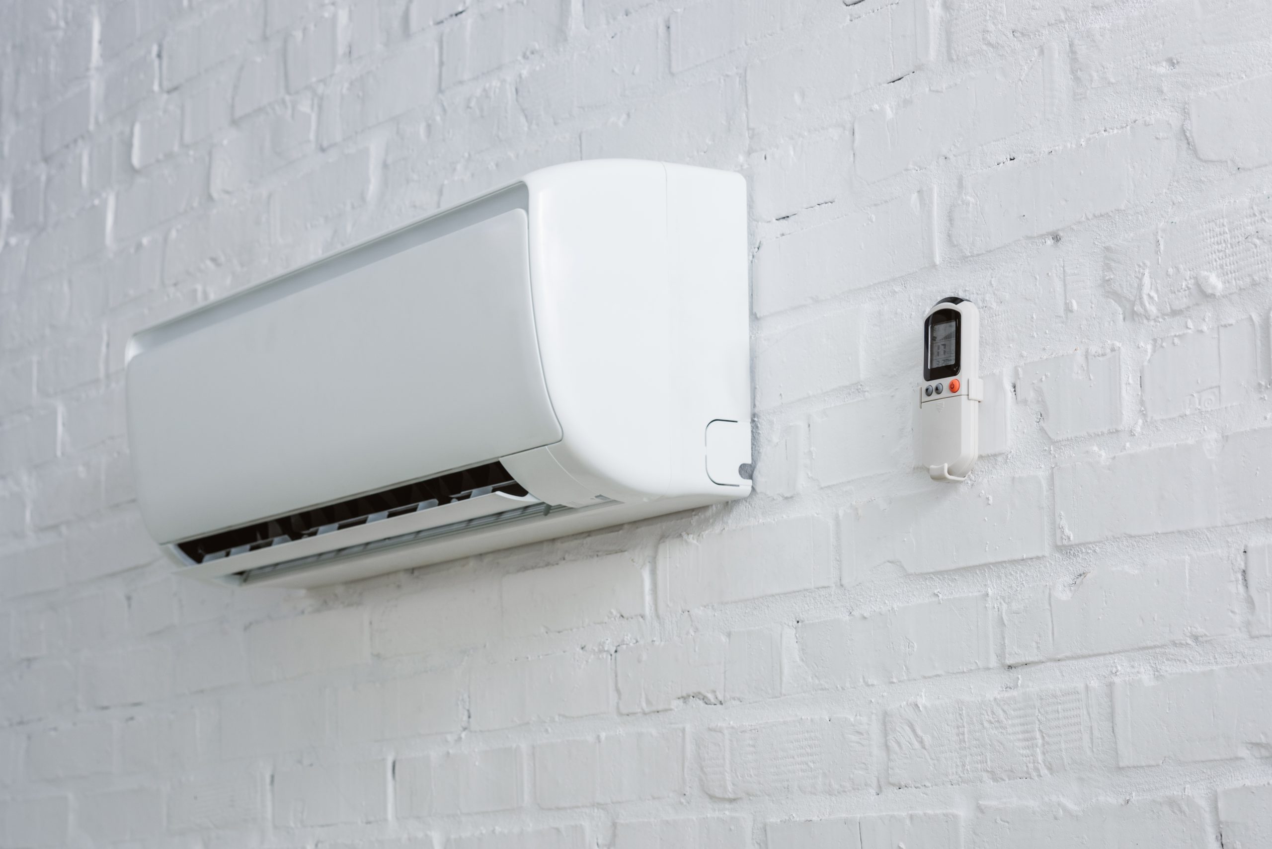 air conditioner hanging on white brick wall with remote control